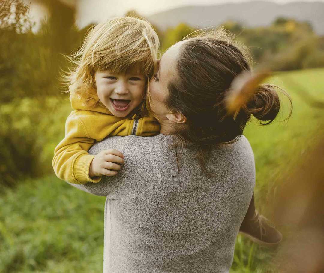 Eine Mutter hält ihr Kind auf dem Arm und küsst es während es lacht